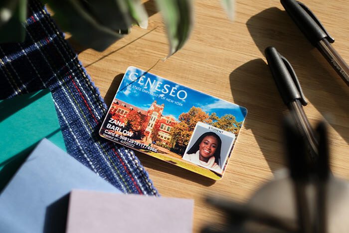 Geneseo Student ID card on a table with assorted sticky notes and pens.