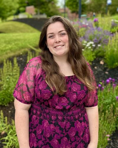 White woman with long brown hair wearing a purple dress