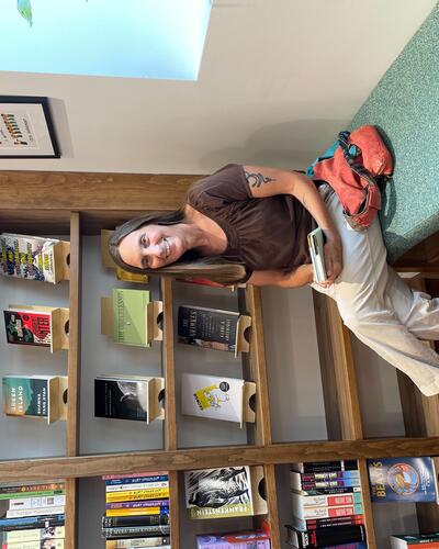 woman sits on green bench, under a window, in front of a bookshelf