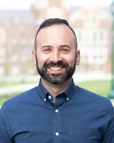 Portrait of Jaime Castillo wearing a blue button-down shirt outside on the quad