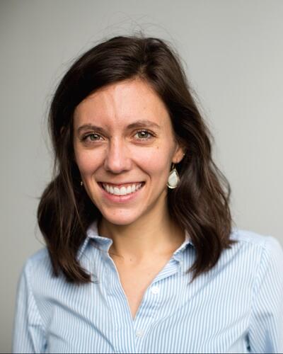 Woman with long brown hair wearing a blue shirt, smiling