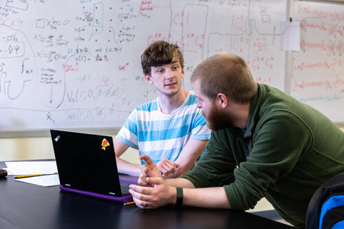 A student speaks with a professor in a physics lab.