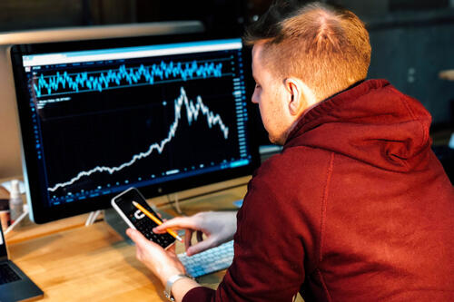 student with cell phone in front of computer screen